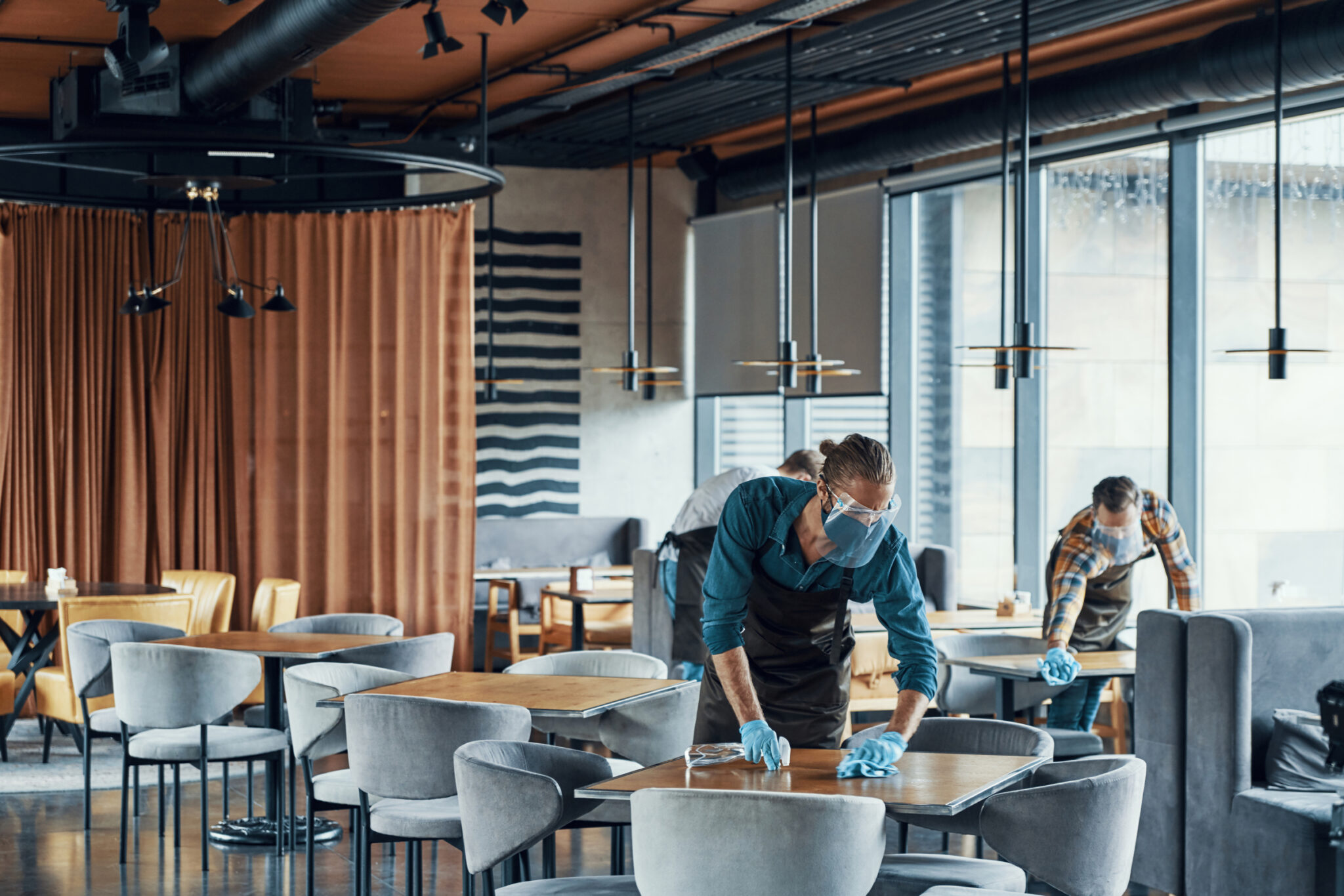 Wait staff in protective workwear cleaning tables in restaurant